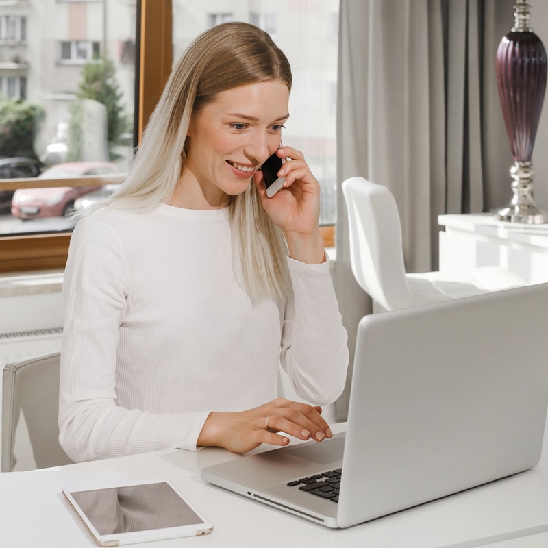 A happy woman talking on her phone with using her laptop